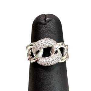 May include: A silver-toned ring featuring a chain-link design. The central links are encrusted with small, clear, sparkling stones, while the outer links remain smooth and polished, creating a contrast between the textured and reflective surfaces.