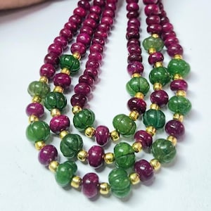 May include: A multi-strand necklace featuring alternating deep magenta and forest green beads. The green beads have a carved, ribbed texture, while the magenta beads are smooth and round. Small, polished gold-tone metal spacer beads are placed between each larger bead throughout the design.