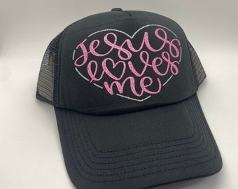 May include: Black trucker hat with a pink glitter heart design that says "Jesus loves me".