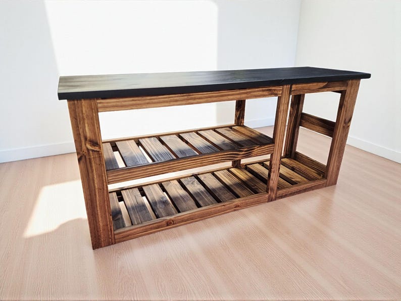 Op de afbeelding: Een houten console met een donker gebeitst blad en twee onderste planken. De tafel is gemaakt van gebeitst hout, met de natuurlijke nerf. De planken zijn voorzien van lamellen en de tafel is ongeveer 152 cm lang.