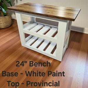 May include: A wooden bench with a white painted base and a provincial-style top. The bench is 24 inches long and features two slatted shelves. The top is a dark brown color.