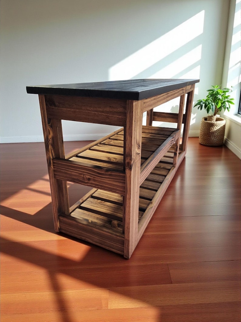 Op de afbeelding: Houten keukeneiland met een donker gebeitst bovenblad en twee onderste planken. Het eiland is gemaakt van massief hout met een natuurlijke afwerking, waarbij de houtnerf zichtbaar is. Het ontwerp is rustiek en functioneel, geschikt voor een keuken of eetkamer. Ongeveer 120 cm lang.