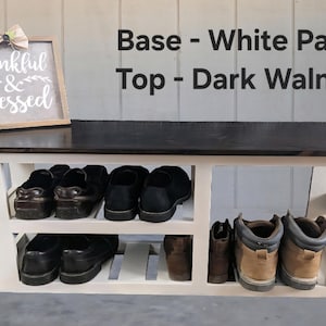 May include: A white-painted shoe rack with a dark walnut top. The rack has two shelves filled with various shoes and boots. A framed sign with the words "thankful & blessed" sits on top. The text "Base - White Paint Top - Dark Walnut" is also visible.