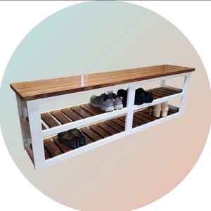 May include: A wooden shoe rack with a white frame and a natural wood top and shelves. The shoe rack has two slatted shelves and is holding several pairs of shoes. The design is simple and functional.