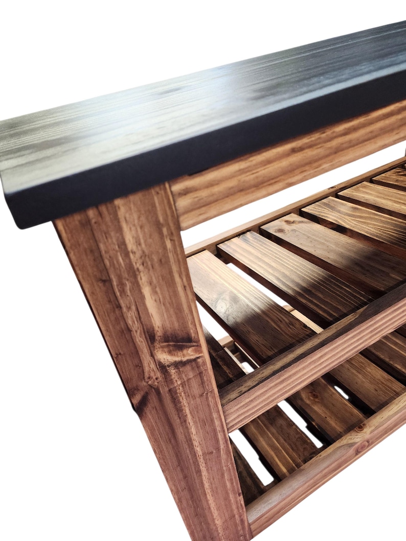 Op de afbeelding: Houten bank met een donkergrijze bovenkant en een onderste plank van houten latten. De bank heeft een natuurlijke houten afwerking met zichtbare nerven en knopen. De poten zijn schuin voor stabiliteit.