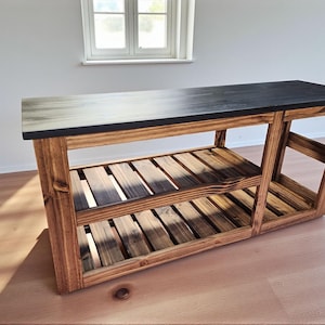 Op de afbeelding: Een houten console met een zwart blad en twee lattenplanken. Het frame is gemaakt van natuurlijk getint hout en het blad heeft een donkere vlek. De tafel is stevig en geschikt voor diverse doeleinden.