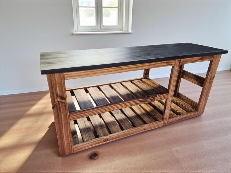 Op de afbeelding: Een houten console met een zwart blad en twee lattenplanken. Het frame is gemaakt van natuurlijk getint hout en het blad heeft een donkere vlek. De tafel is stevig en geschikt voor diverse doeleinden.