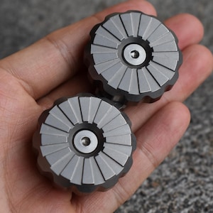 May include: Two silver-colored metal fidget spinners with a textured, circular design. Each spinner has a small, round center hole.