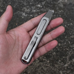 Puede incluir: Una multiherramienta de titanio plateado con una palanca, un abridor de botellas y un destornillador de cabeza plana.