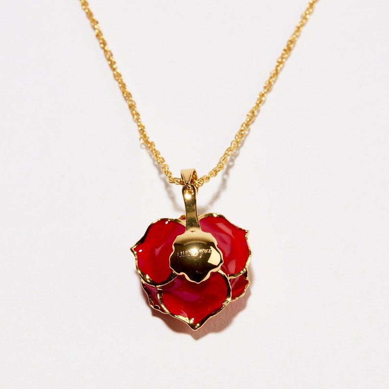 Pode incluir: Um colar de corrente de ouro com um pingente de rosa vermelha. A rosa &eacute; feita de metal e tem um acabamento brilhante, semelhante ao esmalte.
