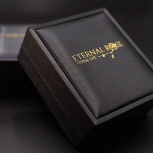 Pode incluir: Uma caixa de presente preta com um logotipo em relevo dourado que diz "Eternal Rose, Eternal Love".