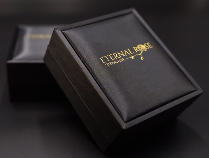 Pode incluir: Uma caixa de presente preta com um logotipo em relevo dourado que diz "Eternal Rose, Eternal Love".