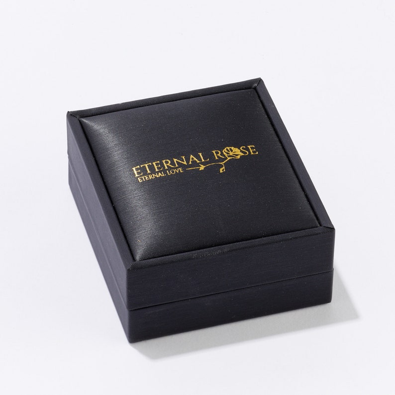 Pode incluir: Uma caixa de joias de veludo preto com as palavras "Eternal Rose" e "Eternal Love" em letras douradas.