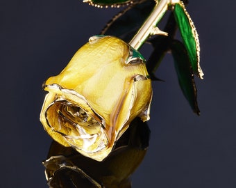 May include: A gold-plated rose with a yellow bloom and green leaves. The rose is detailed with silver accents on the petals and leaves. The stem has thorns and the rose is set against a dark background.