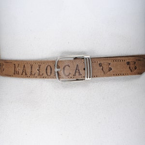 May include: A brown leather belt with the word "MALLORCA" embossed on it. The belt has a silver-colored buckle and decorative embossed images. The belt is displayed on a white mannequin.