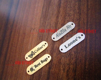 May include: Four gold and silver oval-shaped metal tags with holes for hanging. The tags are engraved with the text "Celine's" with a butterfly, "Best Bags" with a yarn ball and knitting needles, "Alezile Nc" and "Loone's".
