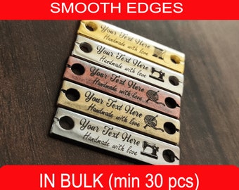 May include: Five metal tags with smooth edges and rounded corners. Each tag has a different color and design. The tags are engraved with the text "Your Text Here Handmade with love" and a small icon. The icons include a sewing machine, a spool of thread, and a ball of yarn.
