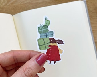 May include: A brown rabbit wearing a red coat and a yellow scarf carries a stack of wrapped green presents.