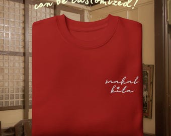 May include: A red crewneck sweatshirt featuring the embroidered white cursive text "mahal kita" with a small heart icon on the right chest area. The text "can be customised!" is printed in a light yellow script font above the garment.