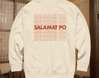 May include: A cream-coloured crewneck sweatshirt featuring the text SALAMAT PO printed in red. The text is repeated in six horizontal lines, with the fourth line appearing in a bold, solid red font while the others are outlined in red.