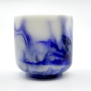 May include: A white ceramic mug with a blue marbled design. The mug has a rounded bottom and a wide, open top.