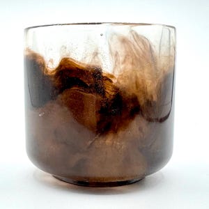 Könnte beinhalten: Eine klare Glasvase mit einem braunen und weißen Marmormuster. Die Vase hat einen runden Boden und eine zylindrische Form.