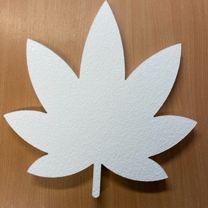 May include: A white, textured leaf shape with five lobes and a stem. The leaf is made of a solid material and is set against a brown wooden surface. The leaf's design is simple and natural.