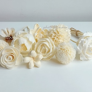 May include: A collection of white sola wood flowers, including roses, carnations, and a plumeria, along with a bouquet of sola wood diffuser sticks.