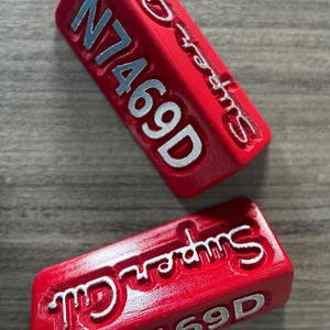 May include: Two red rectangular blocks with the text "Super Groms" and "N7469D" in white lettering.