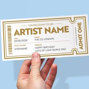 Op de afbeelding: Een rechthoekig evenemententicket met een witte achtergrond en een gouden rand. De tekst luidt: YOU'RE GOING TO SEE, ARTIST NAME, DATE: 20/05/2026, VENUE: THE O2 LONDON, TICKET HOLDER: STEPHANIE, MESSAGE: HAPPY BIRTHDAY LOTS OF LOVE MUM & DAD, ADMIT ONE.