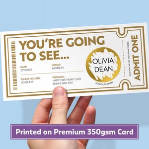 Könnte beinhalten: Ein weißes, rechteckiges Veranstaltungsticket mit goldenen Rändern und dem Text YOU'RE GOING TO SEE, ADMIT ONE sowie einem goldenen Rubbelfeld, das den Namen OLIVIA DEAN enthüllt. Das Ticket enthält Felder für Datum 21/11/2026, Veranstaltungsort Wembley und Nachricht.