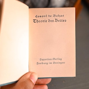 Könnte beinhalten: Ein aufgeschlagenes Buch mit cremefarbenen Seiten und schwarzem Textdruck. Die Titelseite zeigt Honoré de Balzac, Theorie des Bettes, sowie die Verlagsangaben Hyperion-Verlag Freiburg im Breisgau, die unten in einer Serifenschrift gedruckt sind.
