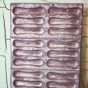May include: A vintage metal baking pan with 24 individual molds for making long, thin pastries. The pan is worn and has a silver-grey finish.