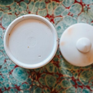 May include: A white ceramic mug with a black handle and the text "But First, Coffee" in a black, handwritten-style font. The mug is on a white surface.
