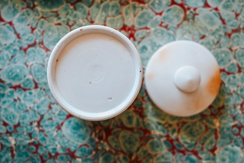 May include: A white ceramic mug with a black handle and the text "But First, Coffee" in a black, handwritten-style font. The mug is on a white surface.