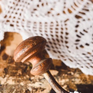May include: A close-up of a wooden hook with a brown finish. The hook is attached to a metal rod and is resting on a white crocheted doily.