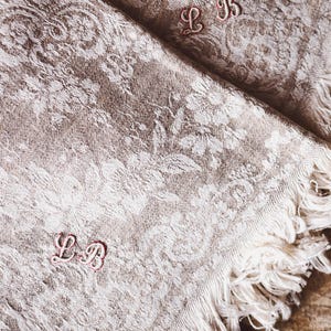 Può includere: Due tovaglioli di lino bianco con bordi sfrangiati e iniziali ricamate "L.B." in filo rosa.