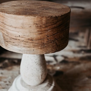 Könnte beinhalten: Ein rustikaler Holz-Sockeltisch mit einer runden, gealterten Holzplatte. Der Sockel ist in einem gesprenkelten, cremefarbenen Farbton gehalten und hat eine bauchige Mitte und einen abgestuften Boden. Der Tisch wird wahrscheinlich zur Präsentation oder als dekoratives Akzentstück verwendet.