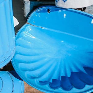 May include: A collection of vintage blue enamelware kitchen items. The image shows a large, shell-shaped wall pocket, a cylindrical container, and a lid. The items are a bright, solid blue color and appear to be made of metal.