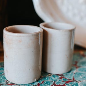 May include: A white ceramic mug with a black handle and the text "But First, Coffee" in a bold, black font. The mug is filled with a dark liquid, likely coffee, and sits on a light-colored surface.