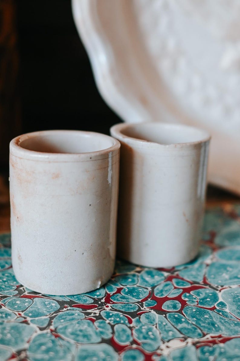 May include: A white ceramic mug with a black handle and the text "But First, Coffee" in a bold, black font. The mug is filled with a dark liquid, likely coffee, and sits on a light-colored surface.
