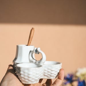 Mostacera de cerámica blanca antigua con diseño de cesta tejida, doble cuenco con cuchara de madera para servir condimentos.