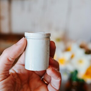 May include: A white ceramic mug with a black handle and the text "But First, Coffee" in a black, bold font. The mug is sitting on a wooden surface. The mug is 4 inches tall.