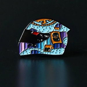 May include: A blue and purple enamel pin of a racing helmet with a number 3 on the side. The helmet has a white and blue striped design with a black visor.