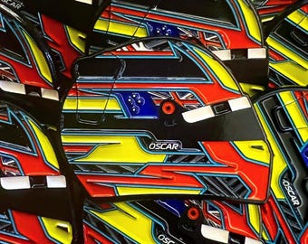 Könnte beinhalten: Nahaufnahme eines Stapels bunter helmförmiger Pins mit dem Wort "OSCAR" auf jedem. Die Pins haben ein schwarz-rot-gelb-blau-weißes Farbschema mit einem karierten Flaggenmuster.