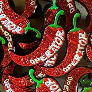 Puede incluir: Primer plano de objetos con forma de chile rojo con la inscripción "Smooth Operator" en blanco. Los chiles tienen tallos verdes y están dispuestos para crear un patrón texturizado y llamativo.