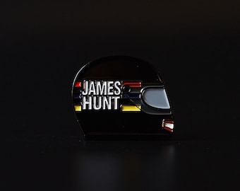 May include: Black enamel pin of a racing helmet with the text "JAMES HUNT" in white letters and red, yellow, and blue stripes.