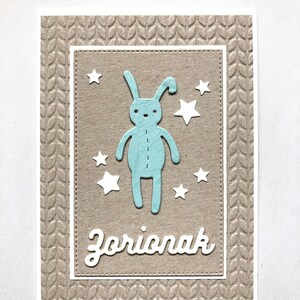 Wenskaart in Baskisch "zorionak", handgemaakt, met een knuffelkonijn en sterren in reliëf.