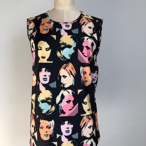 May include: Sleeveless black top featuring a repeating pattern of stylized female faces in various colors, including pink, yellow, and blue. The faces have a pop art style, with bold outlines and geometric shapes. The top is displayed on a mannequin.