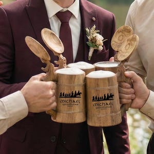 May include: A group of men holding wooden beer steins with the name "Michael" and a silhouette design. The steins are filled with beer and topped with foam. The men are dressed in formal attire, smiling and laughing.